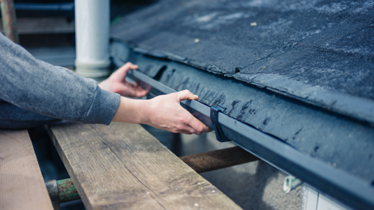 Close up of hands and someone fixing their roof gutters